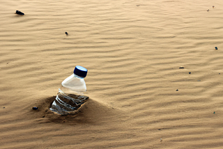 An empty plastic water bottle embedded in the sand in the desert