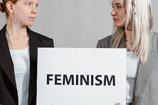 Two white women holding a feminism sign.