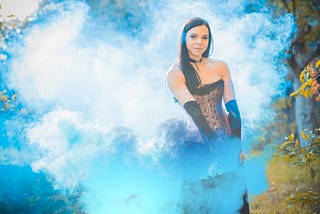 Woman standing in the forest covered in blue smoke — Picture from Depositphotos.com