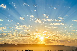 Sunrise over the mountains with blue sky, clouds, and shades of gold