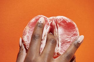 A finger inside a segment of pink grapefruit