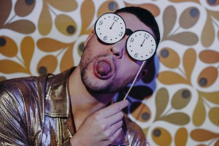 Man sticking his tongue out while holding a clock like sunglasses