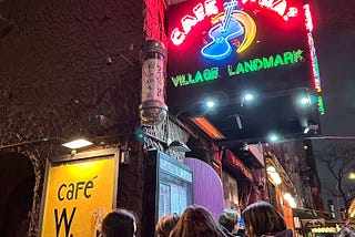 Night scene with neon lights of Cafe Wha? with group of people waiting to get in
