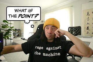 A man wearing a “Rage Against the Machine” t-shirt sits and looks to the side; a thought-bubble next to him reads, “What is the point?”