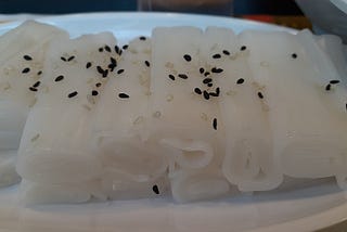 Rolled white rice noodle roll sprinkled with black sesame seeds.