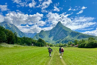 Image of Author’s husband and friends walking the Juliana Trail in a green meadow with alps in the background.