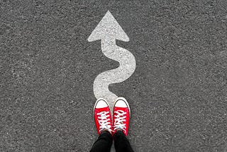 A person stands on a curvy arrow painted on the street.