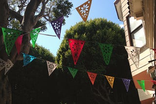 Multi-colored streamer flags in a tree-lined neighborhood with blue skies