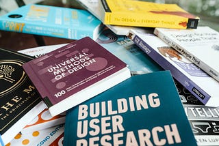 A messy pile of books about UX, including Universal Methods of Design and Building User Research