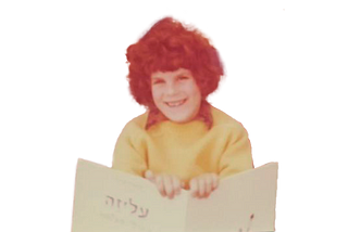 Adva Shaviv at age 7, smiling while holding up a book.