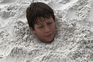 young boy buried in sand at the beach