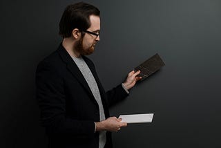 A man in a suit jacket holding up two different blocks and tiles and looking in comparison