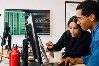 (Article written by @Coursera) — [Featured image] Two cybersecurity consultants collaborate at a shared workstation.