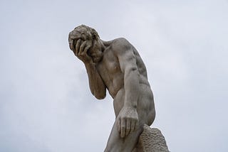 A statue of a male doing a face-palm against a cloudy-sky background