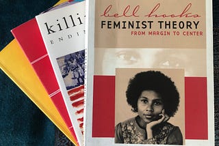 a small stack of four books by bell hooks. The book, “Feminist theory from margin to center” is on the top with a photo of a young bell hooks looking at the camera.