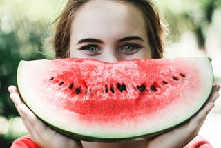 Smiling young woman holding a big watermelon “smile” in front of her mouth