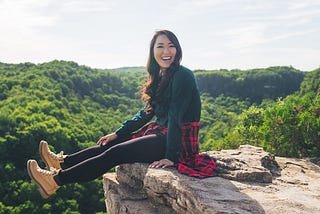 Lisa Le sits on a rocky bluff overlooking a lush forest.