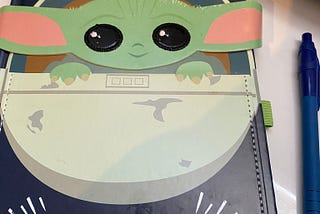 Baby Yoda notebook with title “I’m all ears” on a white desk next to a blue gel pen.