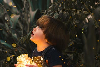 Child gaping upward, holding glass jar with string of bright white lights inside