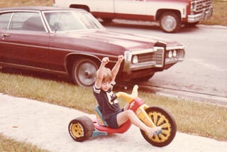 Author as a child riding a big wheel on a neighborhood sidewalk, circa 1980s.