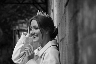 Girl in a tiara leans against a wall with a smile.