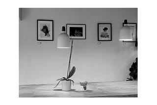 A picture taken by the writer at a cafe with a flower vase of the table, two hanging lamps and artworks on the wall.