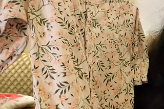 A small floral baby onesie on a hanger being held up indoors.