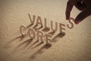 CORE VALUE wood word on compressed or corkboard with human’s finger at S letter