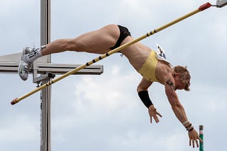 An athlete vaulting over a bar against cloudy background