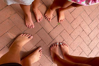The barefoot feet of four children standing together on a brick patio