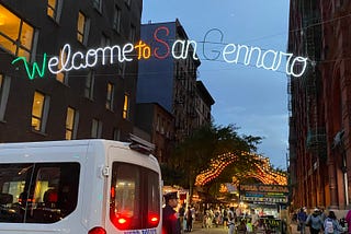 The view south down Mulberry Street from Houston, showing the Feast of San Gennaro and a neon sign reading “Welcome to San Gennaro”