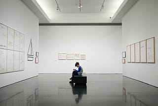 A child sitting on a bench in a minimalist art gallery.