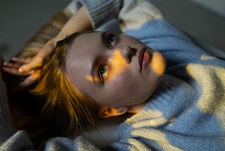 Woman in blue sweater lying on bed.