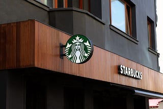 A wooden storefront with a logo of Starbucks — my favorite coffee shop. Camille Allard on Medium.com.