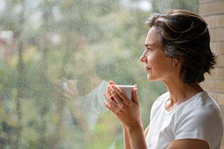Pensive woman drinking from cup looking out a window