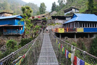 Me waving and standing on the other side of a suspension bridge in Nepal