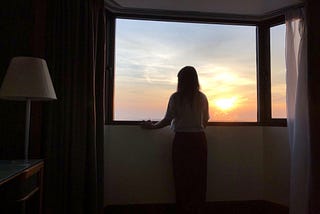 A young woman looks out a window at sunset