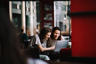 Two women smiling looking at a computer together
