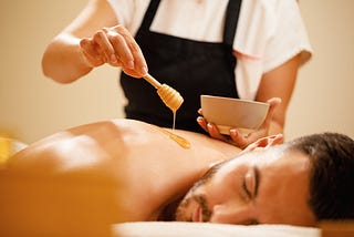 Close-up of therapist pouring honey during back massage at spa salon.