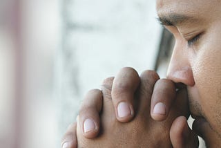 Depressed man sitting in room praying, thoughtful, mindful, unease, worry.