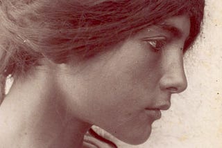 A vintage black and white photograph of a young, dark-haired woman with eyes fixed on something to the right of the frame.