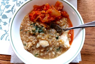 Overhead shot of a bowl of rice porridge with fish and kimchi.
