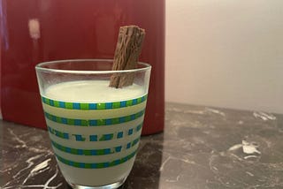 A Cadbury’s Flake in a glass of chilled milk. The glass has green stripes and is placed on a black and white marble table, with a red lamp in the background.