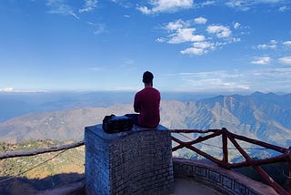A guy sitting at a mountain top overlooking mountains