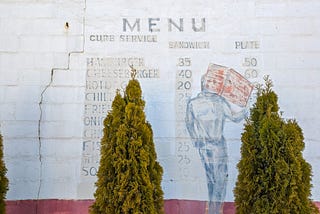 Painted brick wall showing a faded restaurant menu with outdated food prices