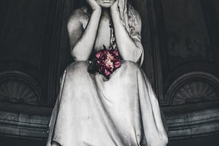 A marble carving of a woman sitting, elbows on knees, hands supporting her head, flowers in her lap.