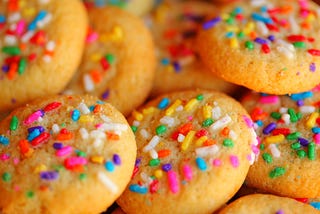A pile of fresh-baked sugar cookies with rainbow sprinkles on them.