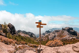 Sign posts pointing multiple directions in the middle of a rocky mountain path.