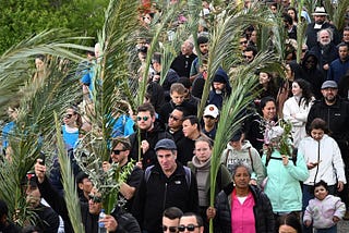 A diverse crowd of people walk carrying palms in a Palm Sunday procession.