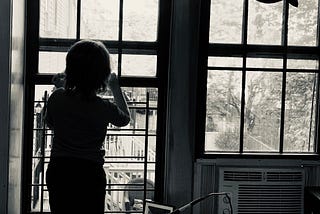 Black and white picture of a kid looking outside a window.